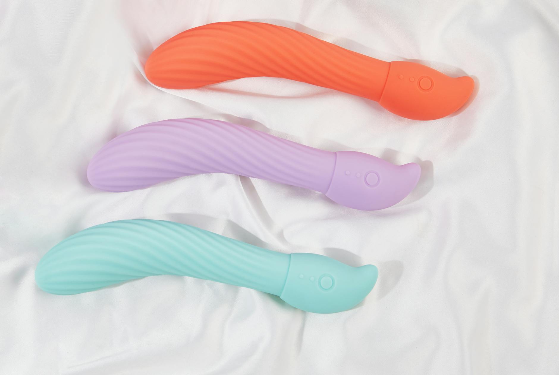 Three colorful vibrators arranged on white fabric, highlighting their smooth texture and design