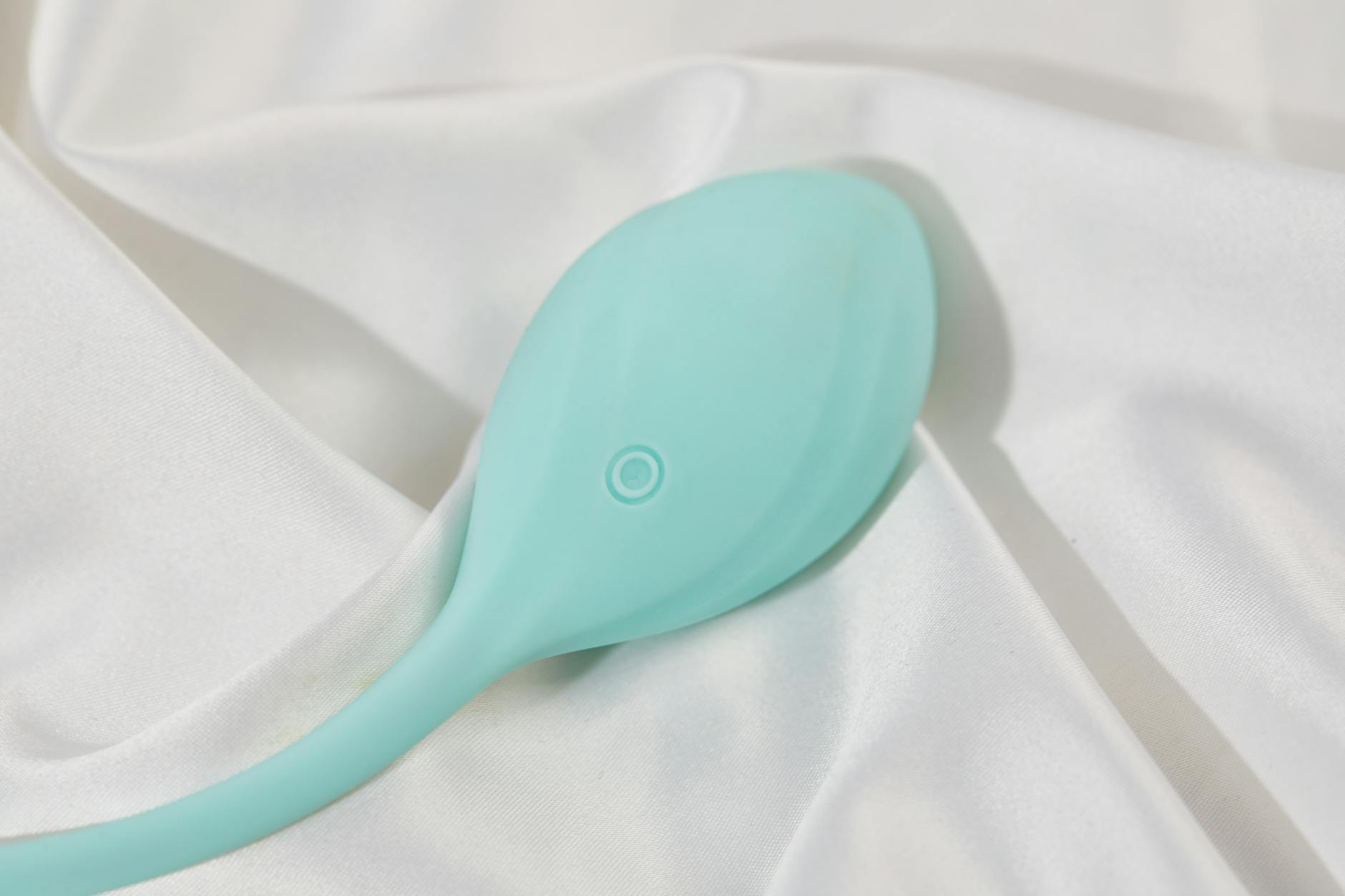 A sleek teal lemon clitoral vibrator on soft white silk fabric, symbolizing self-care and personal rediscovery after heartbreak.