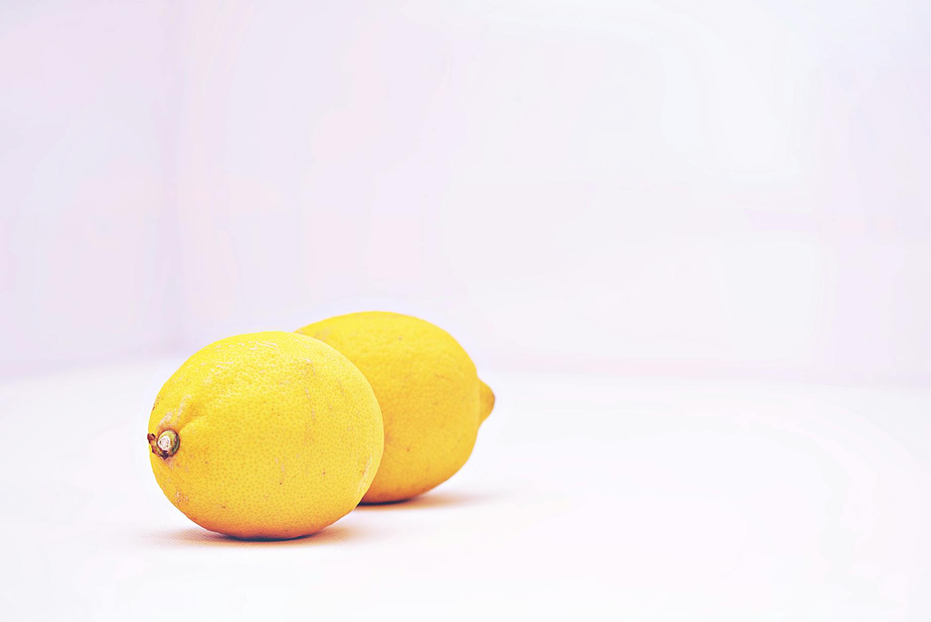 Two vibrant lemons against a minimalist white background, symbolizing the fresh, uncomplicated design of lemon vibrators.