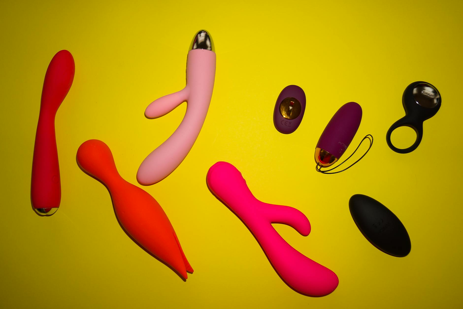 Colorful sex toys arranged on a yellow surface, showcasing vibrator options and design variety